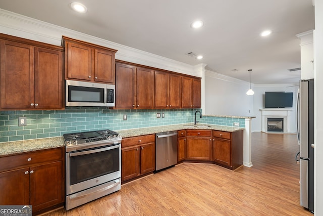 kitchen with appliances with stainless steel finishes, light wood-style floors, ornamental molding, a sink, and a peninsula