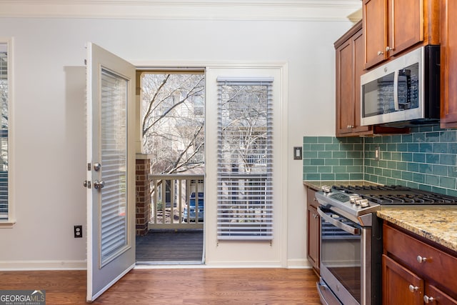 kitchen featuring appliances with stainless steel finishes, wood finished floors, light stone counters, and decorative backsplash