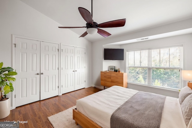 bedroom featuring visible vents, ceiling fan, wood finished floors, vaulted ceiling, and two closets