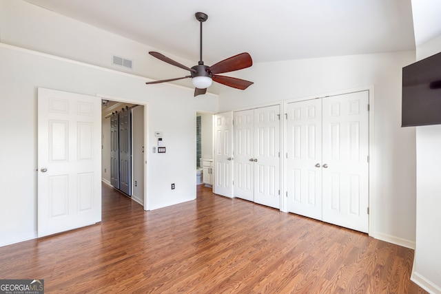 unfurnished bedroom with two closets, lofted ceiling, visible vents, ceiling fan, and wood finished floors