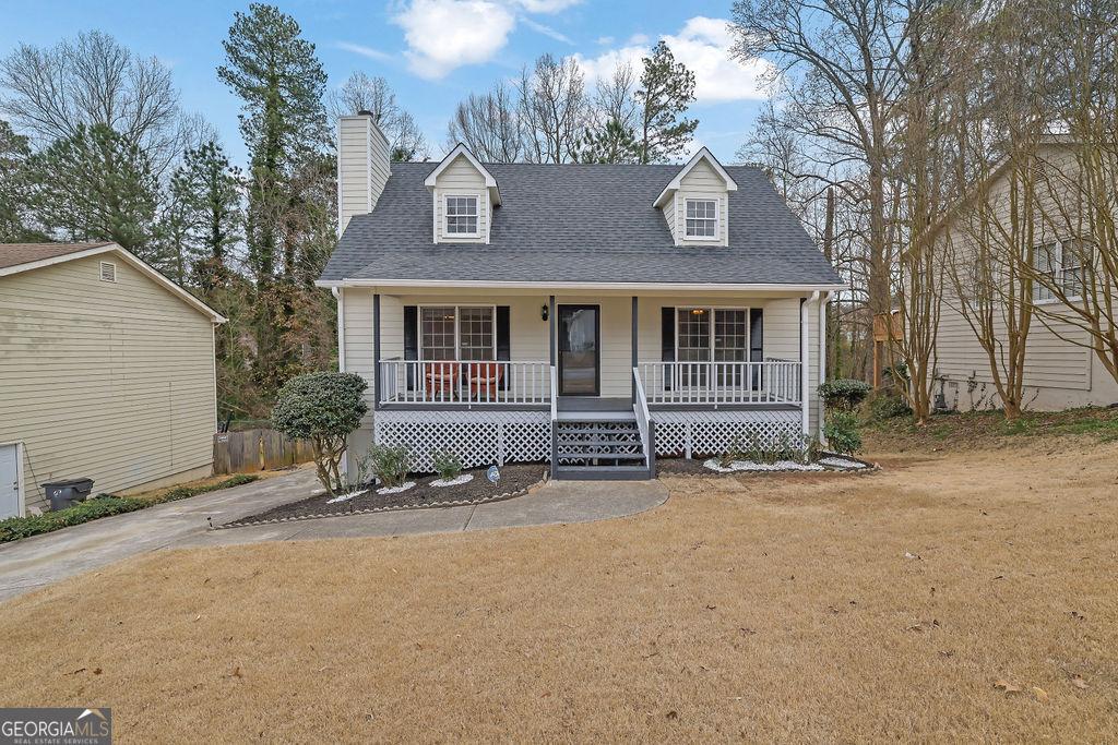 cape cod-style house featuring a shingled roof, a chimney, a front lawn, and a porch