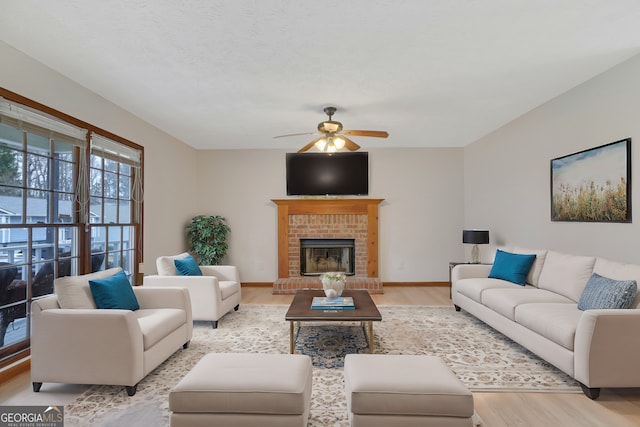 living area with a ceiling fan, a fireplace, light wood-style flooring, and baseboards