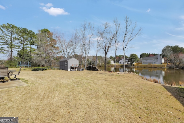 view of yard featuring an outbuilding, a shed, a trampoline, and a water view