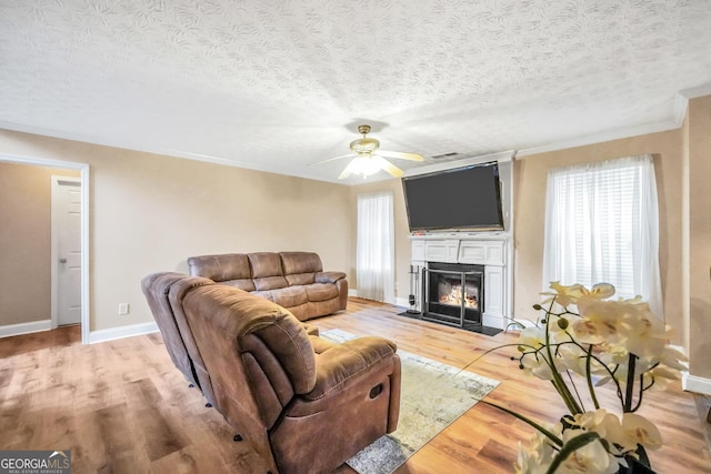 living area with light wood-style flooring, baseboards, a textured ceiling, and a fireplace with flush hearth