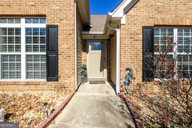 view of exterior entry with brick siding and a shingled roof