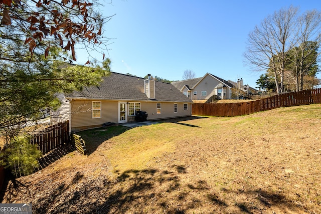 rear view of house featuring a yard, a shingled roof, a chimney, and a fenced backyard