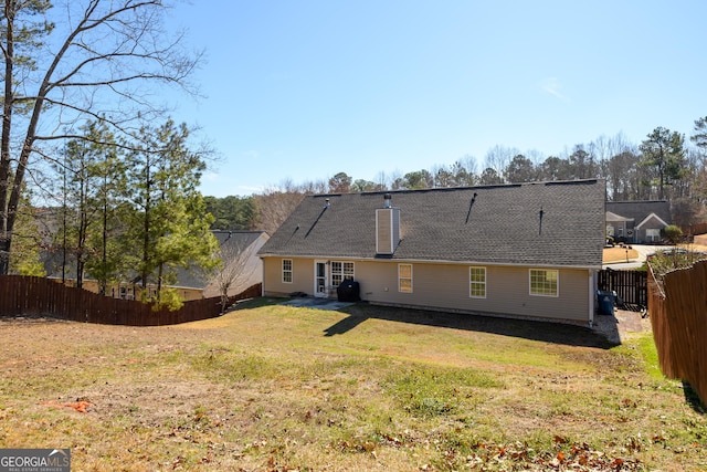 rear view of property featuring a fenced backyard, a yard, and a chimney