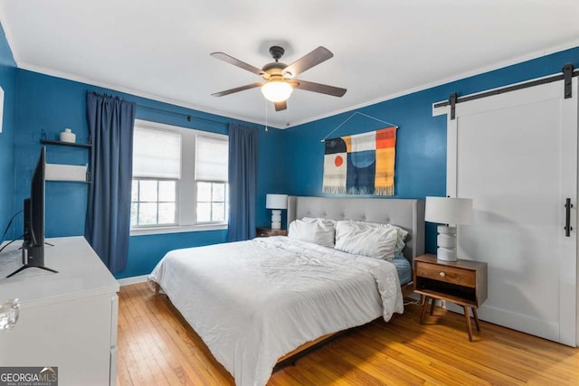 bedroom with a barn door, baseboards, wood-type flooring, and a ceiling fan