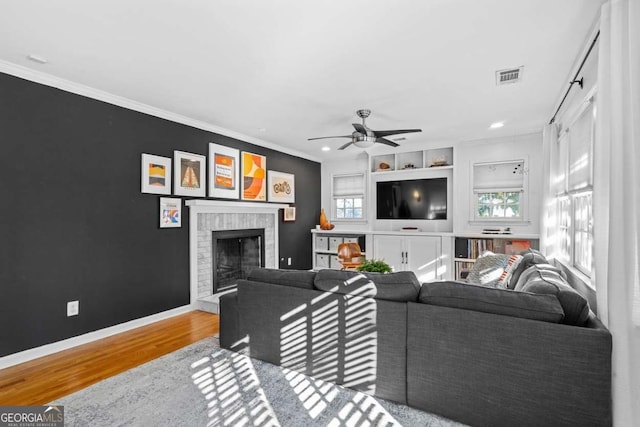 living area with wood finished floors, visible vents, baseboards, a brick fireplace, and crown molding