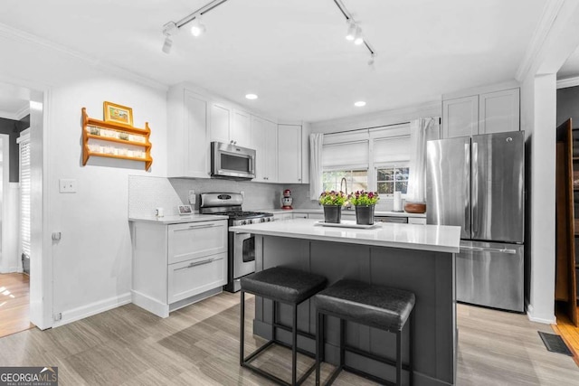 kitchen featuring stainless steel appliances, light countertops, crown molding, and a breakfast bar area