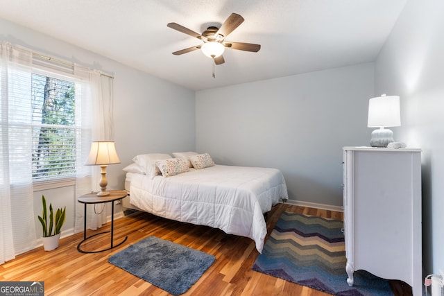 bedroom with ceiling fan, wood finished floors, and baseboards