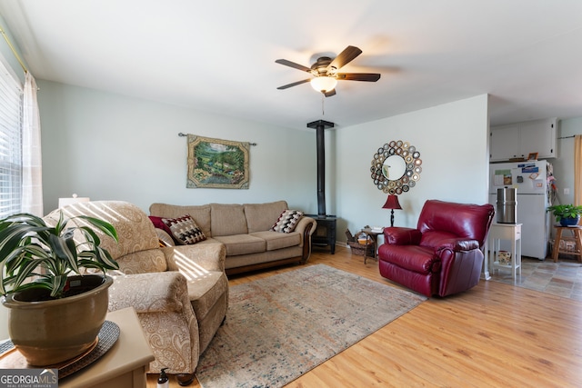 living room featuring ceiling fan, light wood-style flooring, and a wood stove