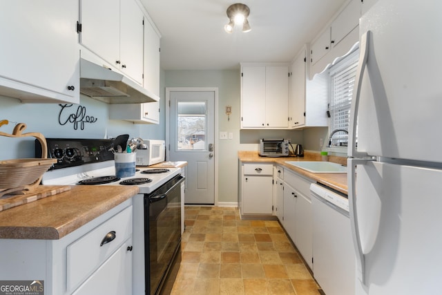 kitchen with stone finish floor, white appliances, white cabinets, and a sink