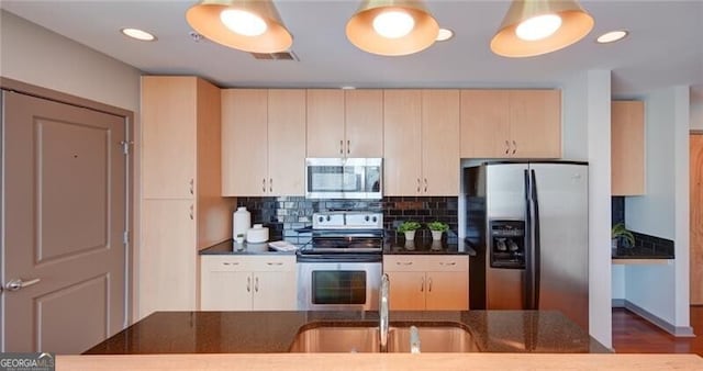 kitchen featuring stainless steel appliances, a sink, visible vents, backsplash, and dark stone countertops