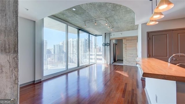 unfurnished living room with a view of city, floor to ceiling windows, arched walkways, and wood finished floors