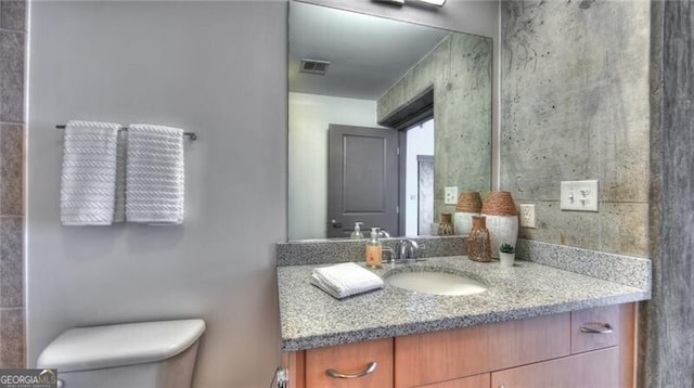 bathroom with toilet, visible vents, and vanity