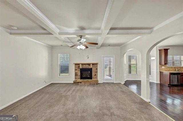 unfurnished living room featuring a stone fireplace, beamed ceiling, and plenty of natural light