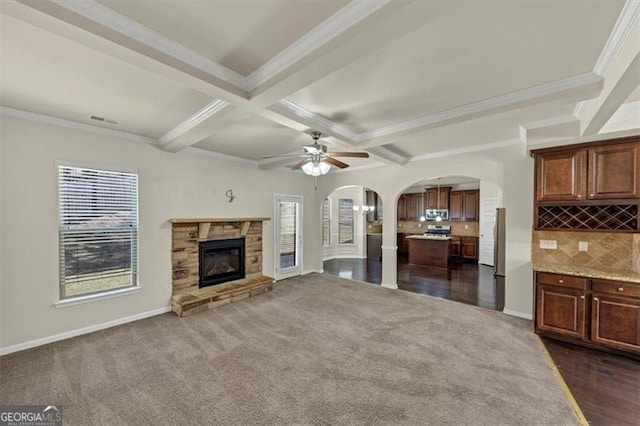 unfurnished living room with arched walkways, coffered ceiling, a fireplace, dark carpet, and beam ceiling