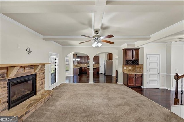 living area with arched walkways, ceiling fan, a stone fireplace, dark wood finished floors, and crown molding