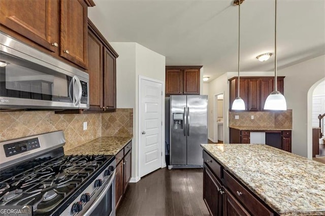 kitchen featuring stainless steel appliances, arched walkways, dark wood-type flooring, and light stone counters