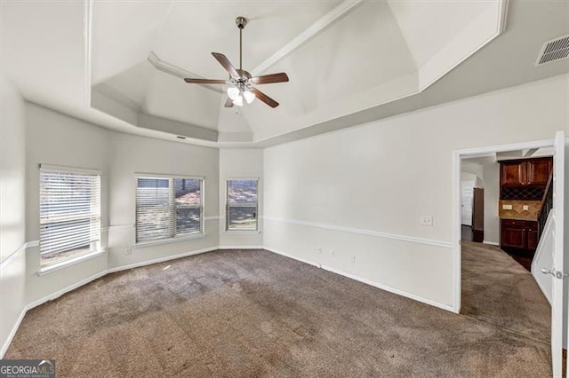 carpeted spare room featuring ceiling fan, a tray ceiling, visible vents, and baseboards