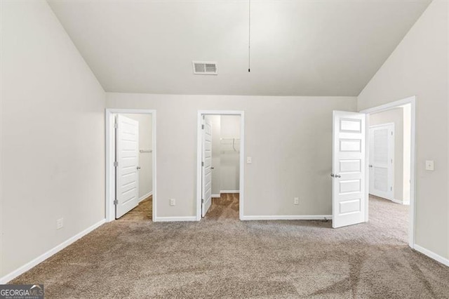 unfurnished bedroom with baseboards, visible vents, lofted ceiling, a spacious closet, and carpet floors