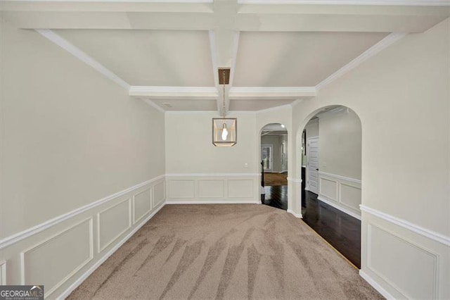 unfurnished dining area featuring arched walkways, a decorative wall, coffered ceiling, wainscoting, and beam ceiling