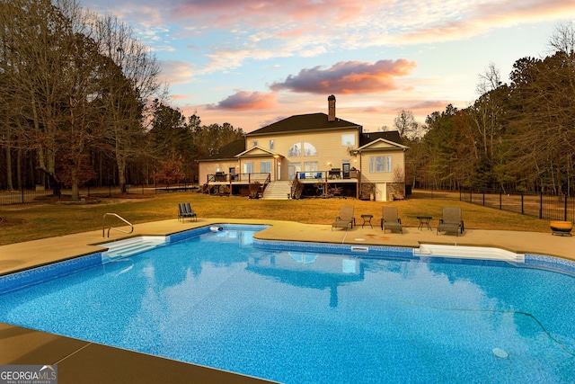 pool at dusk featuring a yard, a patio area, fence, an outdoor pool, and a wooden deck