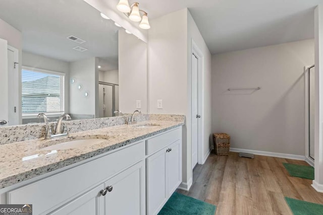 bathroom with double vanity, a sink, a shower stall, and wood finished floors