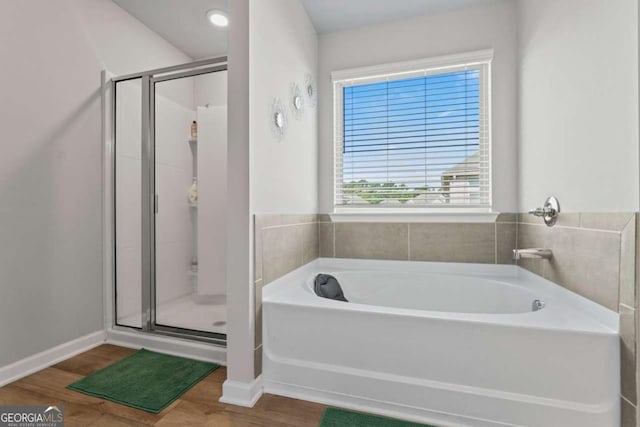 bathroom with a garden tub, a shower stall, baseboards, and wood finished floors