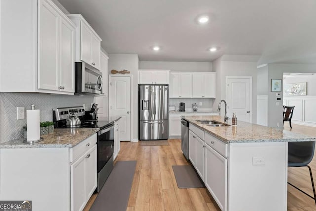 kitchen with a breakfast bar, a sink, white cabinetry, appliances with stainless steel finishes, and light wood finished floors