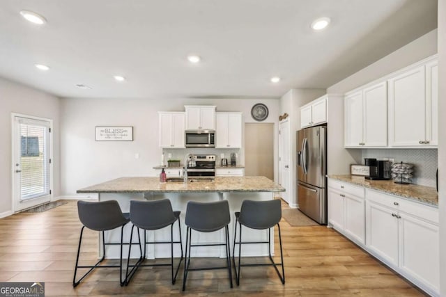 kitchen featuring white cabinets, light wood finished floors, stainless steel appliances, and a kitchen breakfast bar