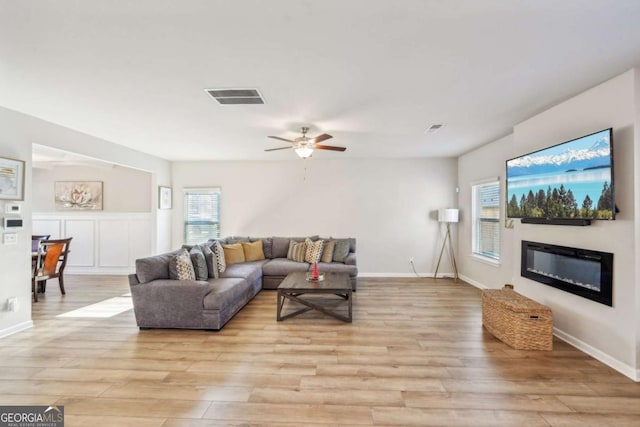 living area with light wood-type flooring, a glass covered fireplace, and plenty of natural light