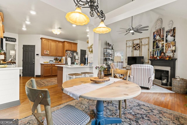 dining room with lofted ceiling with beams, visible vents, a ceiling fan, light wood finished floors, and a glass covered fireplace