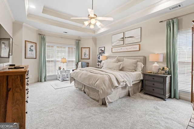 carpeted bedroom with baseboards, visible vents, a ceiling fan, a tray ceiling, and crown molding