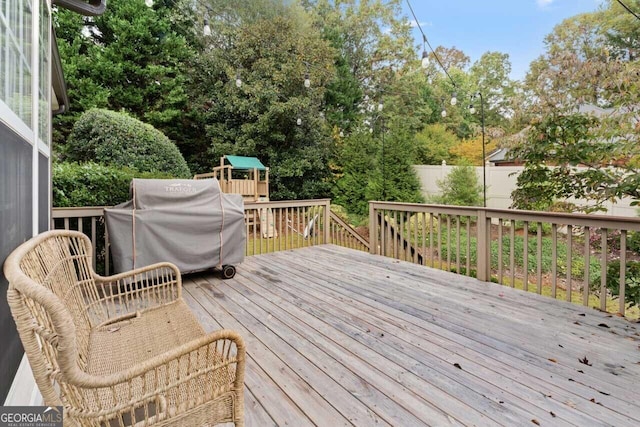 wooden terrace with a grill, fence, and a playground