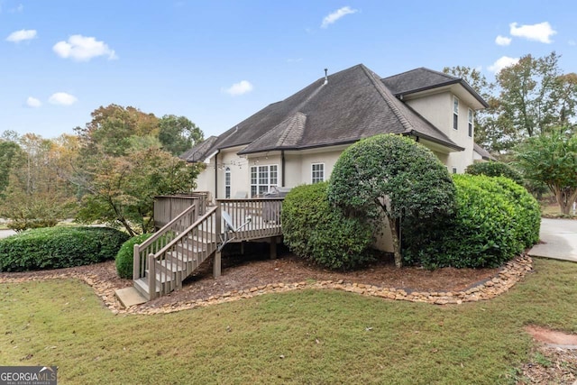 back of property with a shingled roof, a lawn, stairway, a wooden deck, and stucco siding