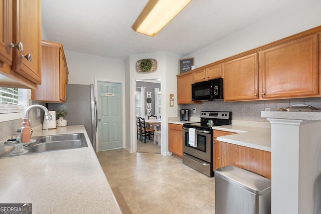 kitchen with brown cabinets, light countertops, decorative backsplash, appliances with stainless steel finishes, and a sink