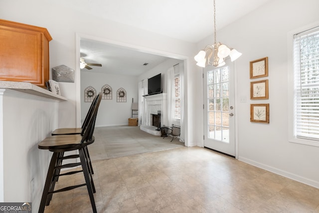 unfurnished dining area with ceiling fan with notable chandelier, a brick fireplace, and baseboards