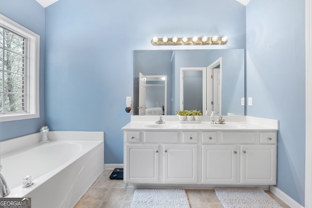 ensuite bathroom with double vanity, baseboards, a sink, and a bath