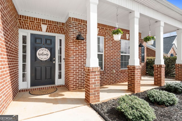 doorway to property with covered porch and brick siding