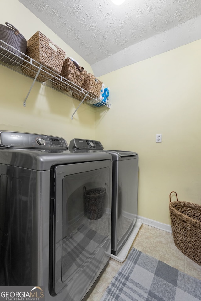 clothes washing area with washing machine and clothes dryer, light tile patterned floors, a textured ceiling, laundry area, and baseboards