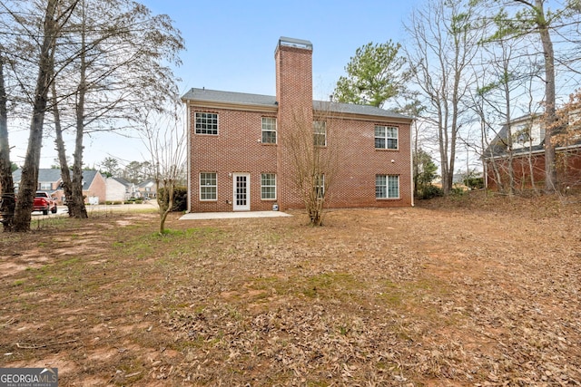 back of house featuring brick siding, a chimney, and a patio area