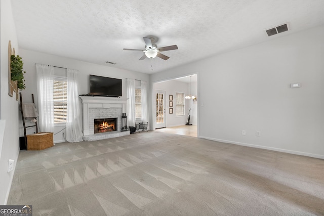 unfurnished living room featuring a brick fireplace, visible vents, a ceiling fan, and light colored carpet