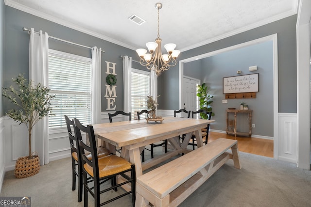 dining room with light carpet, crown molding, visible vents, wainscoting, and an inviting chandelier