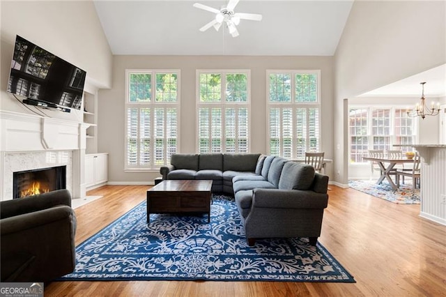 living area featuring a fireplace, wood finished floors, high vaulted ceiling, baseboards, and ceiling fan with notable chandelier