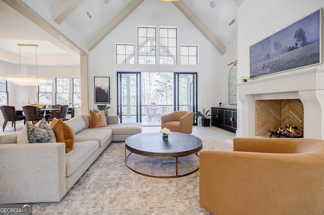 living room featuring beamed ceiling, visible vents, high vaulted ceiling, light wood-style flooring, and a warm lit fireplace