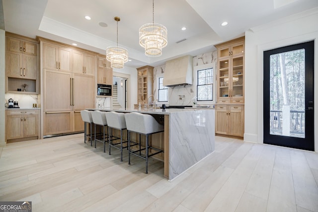 kitchen featuring a spacious island, light brown cabinets, a raised ceiling, and premium range hood