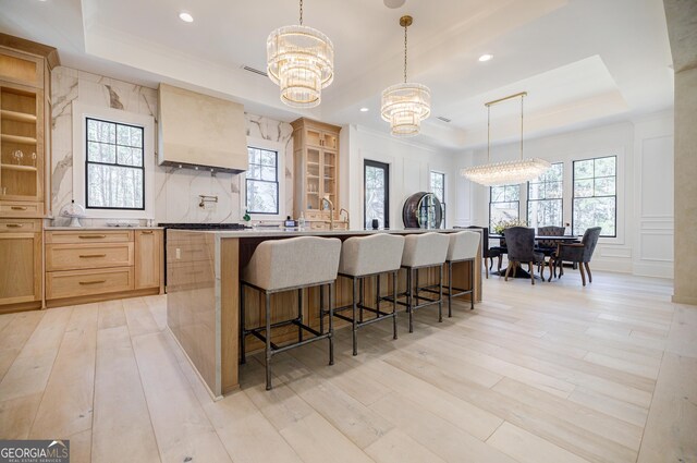 kitchen featuring light brown cabinets, a tray ceiling, light wood-style flooring, tasteful backsplash, and a chandelier