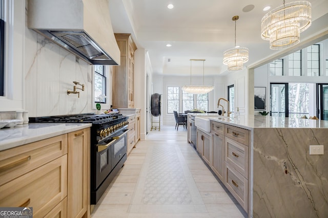 kitchen featuring a chandelier, range hood, light brown cabinets, and range with two ovens